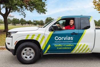 A white truck with a driver inside, the truck is branded with the Corvias Property Management logo.
